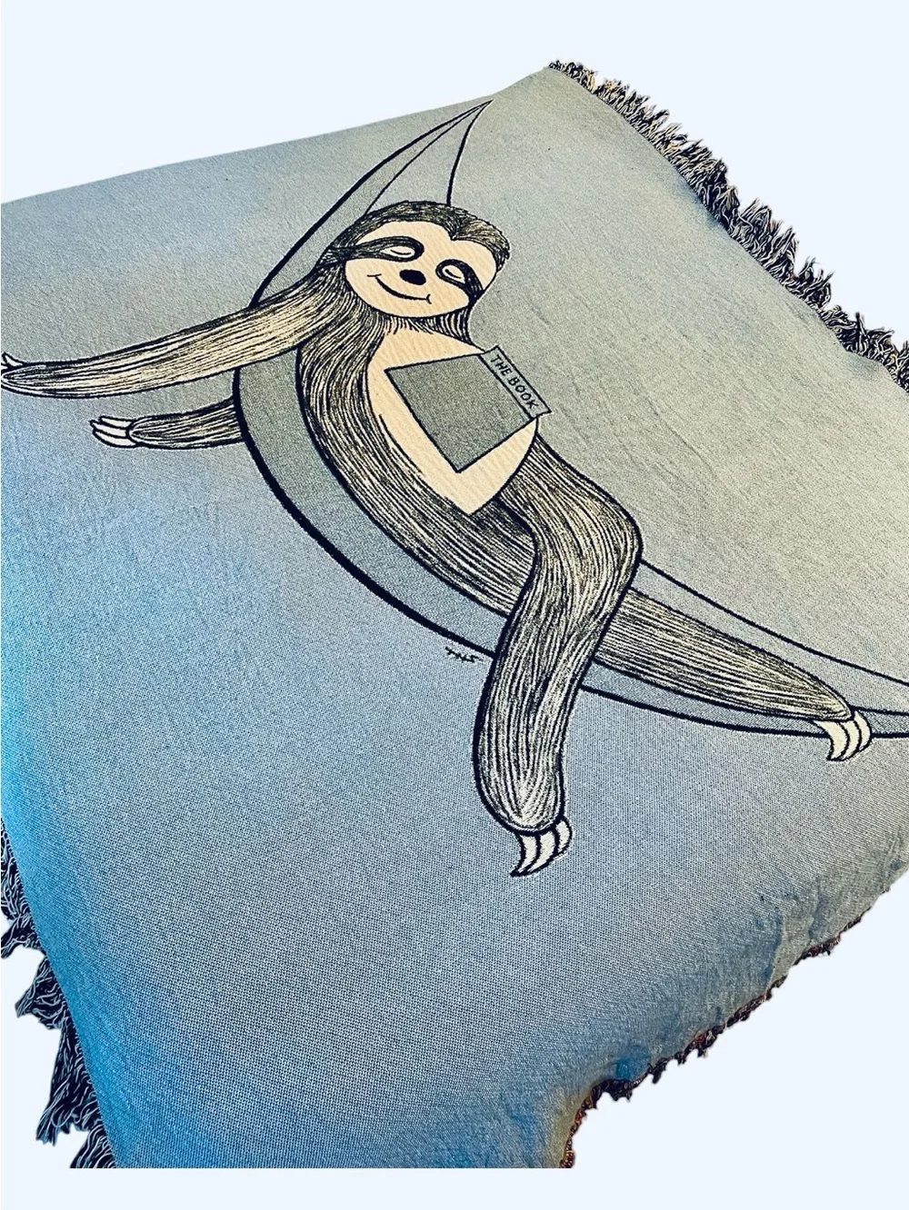 Outcasty cotton throw, relaxing sloth with book, shown on a Queen size bed